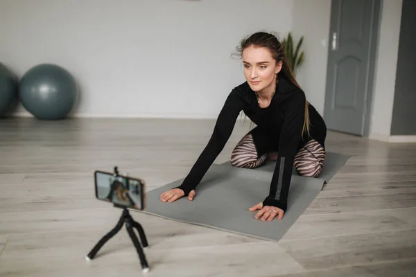 Genç yoga ustası, internetteki kursu için cep telefonuyla yaptığı egzersizin video içeriğini kaydediyor. Stüdyoda atletik kadın eğitimi — Stok fotoğraf