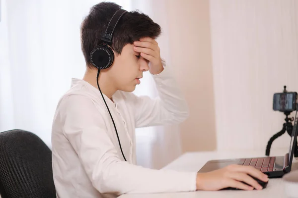 Face palm of teenage steammer during the game. Boy in headphones play on laptop at home