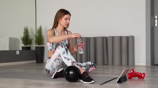 Femeia atletică în îmbrăcăminte sport face exerciții acasă. Femeia se odihneşte, bea apă. Conceptul de sport și recreere. Un stil de viață sănătos — Videoclip de stoc