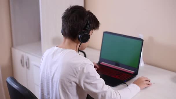 Tenåringsgutt spiller spill på PC-en sin i hvitt rom. Gamer opptak video på web kamera på bærbar datamaskin og telefon på stativ – stockvideo