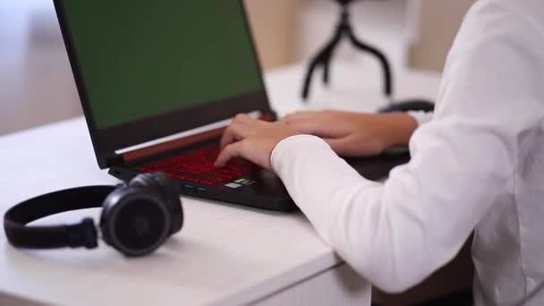 Detailní záběr dospívajícího chlapce, jak hraje hru na počítači v bílém pokoji. Gamer zachytit video na webové kameře na notebooku. Zaměření na stisky tlačítek na klávesnici — Stock video