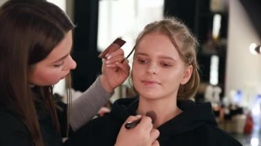 Stüdyodaki çekici sarışın kadın için makyaj yapıyor. Makyaj sanatçısının güzel bir model için kozmetik uyguladığı bir video.