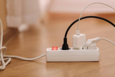 White cable connector for overloaded power boards at home. Close up focus at a plug foreground.