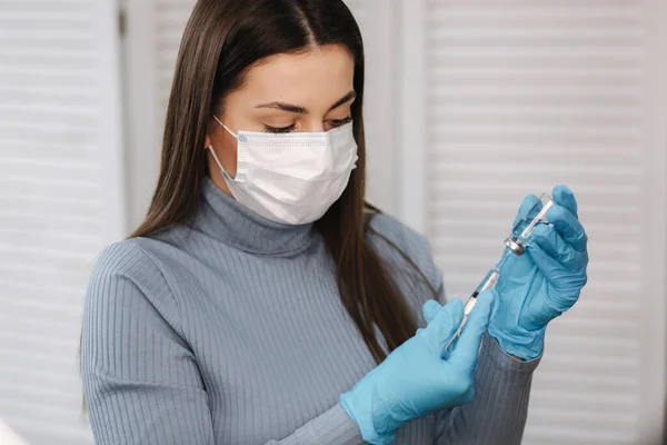 Vaccine in hands, female doctor holds syringe and bottle with covid19 vaccine for coronavirus cure. Concept of corona virus treatment, injection. Female in medical mask