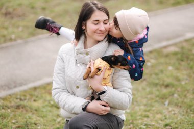 Güzel, genç bir anne kızı ve küçük bir köpekle yürüyor. Mutlu bir aile karantina sırasında evcil hayvanla dışarı çıkıyor.