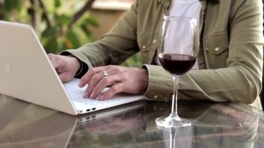 Close up of man wotking using laptop and dring wine outside. Middle selection of working proces. Alcohon during work. Freelancer