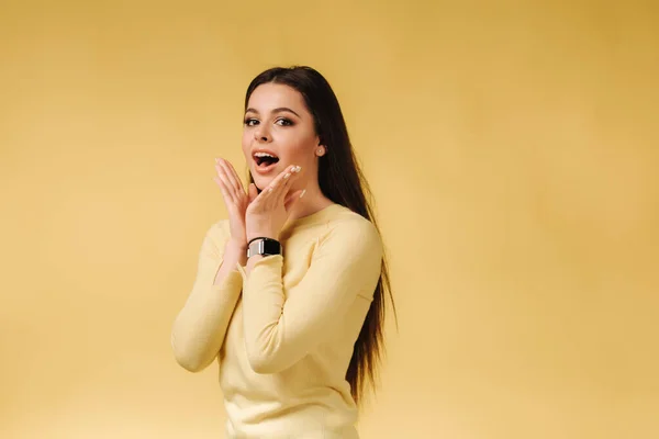 Happy surprised woman in yellow sweatshirt posing to photographer. Portrait of pretty woman on yellow background. Pantone