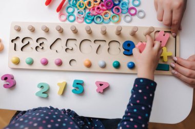 Çocuklar için eğitici bir oyunda oynayan küçük bir kızın en iyi görüntüsü. Farklı renkler ve sayılar içeren tahta bir oyun. Zeki çocuklar için intekaktif oyun. Çocuklar ahşap heykelciği elleriyle dikiyorlar.