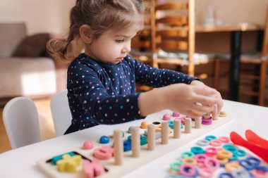 Küçük kız çocuklar için eğitici bir oyun oynuyor. Farklı renkler ve sayılar içeren tahta bir oyun. Zeki çocuklar için intekaktif oyun. Kız karantina sırasında evde vakit geçirmiş.