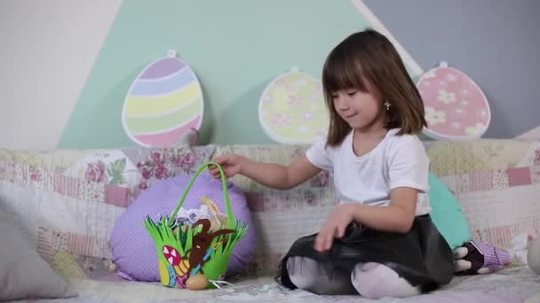 Petite fille mignonne se préparant pour Pâques pendant la quarantaine. Une fille à la maison. Le gamin est assis sur le canapé et fait un panier de Pâques — Video