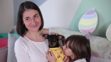 Küçük kız ve annesi evde köpekle oynuyorlar. Mutlu aile Paskalya için hazırlanıyor. Çekici genç anne küçük kızını ve köpeğini seviyor.