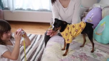 Genç kız fotoğrafçı, annesinin evde köpekle oynarken fotoğrafını çekiyor. Çocuklar için oyuncak kamera