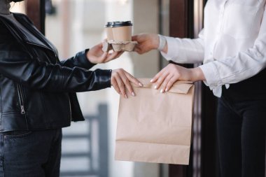 Dışarıdaki maskeli müşteri kahve ve kahve paketini kahve maskesindeki kasiyerden alıyor. Yemeği götür. Karantina