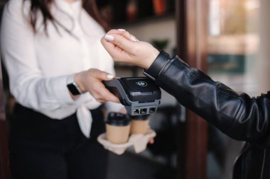 Kablosuz ya da temassız ödeme yapan kadın müşteri. Kasiyer NFC teknolojisi üzerinden ödeme kabul ediyor. Karantina sırasında maskeli iki kişi. Covid19