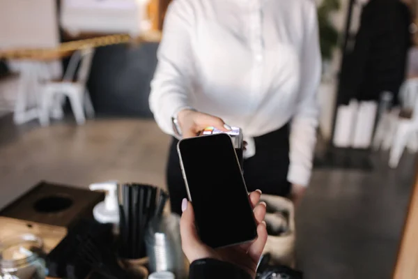 First person view of human hand hold smart phone for payment by NFC at the cafe. Closeup of female hand that giving terminal for online payment