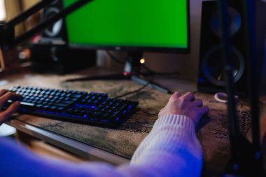 Evde bilgisayar oyunu oynayan ve canlı yayın yapan kulaklıklı genç adam. Teknoloji, oyun, eğlence. Kromakey. Elle fareye yakın çekim