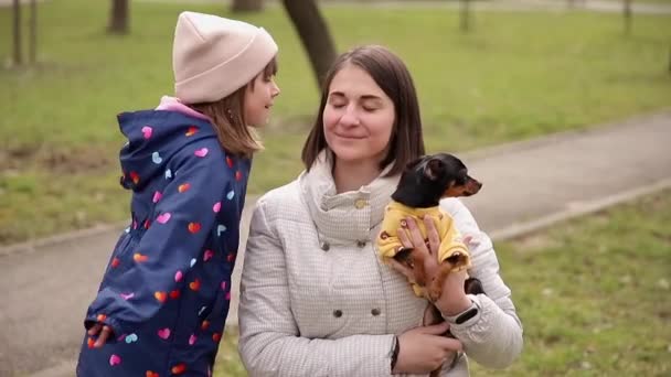 Belle jeune maman marche avec sa fille et son petit chien. Famille heureuse marchant à l'extérieur avec animal de compagnie pendant la quarantaine. Fille embrasser maman — Video