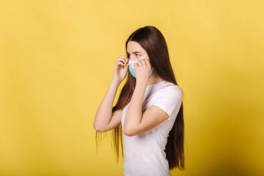 Tıbbi maskeli genç bir kadının portresi sarı arka planda duruyor. Kadın koruyucu maske takmış. Karantina Kapsamlı 19
