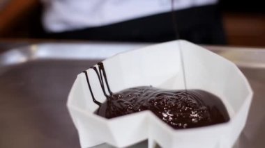 Şekerleme uzmanı macun bıçağı kullanarak erimiş çikolatayla çalışıyor. Pembe eldivenli kadın pasta için tatlı taban hazırlıyor. Yakın çekim sütlü çikolatayı karıştırır.