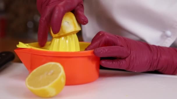 La donna in guanti spreme il succo da limone su cucina. Il primo piano di mani umane fa il succo di limone fresco — Video Stock