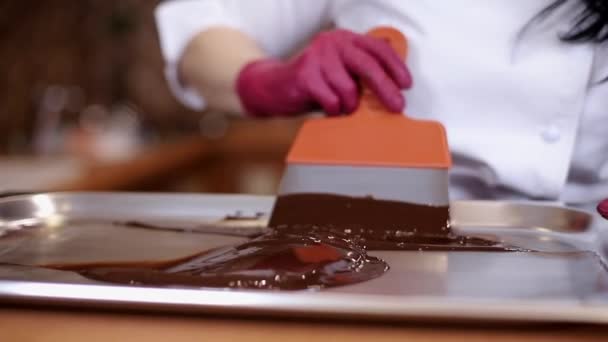 Konditor arbeitet mit Spachtelmesser mit geschmolzener Schokolade. Frau in rosa Handschuhen, die süßen Boden für Kuchen backt. Nahaufnahme mischt Milchschokolade — Stockvideo