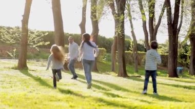 Çocuklarla aktif yürüyüş. Anne ve babanın mutlu aileleri dışarıda çocuklarla vakit geçiriyor. Genç anne ve babasıyla ağaç çocukları koşup zıplıyorlar.