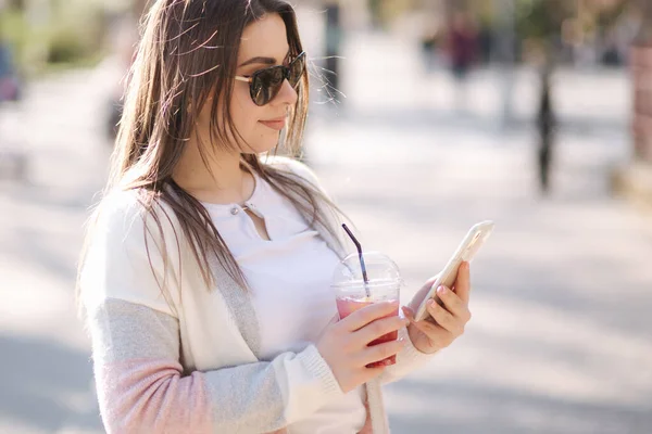 Mooie vrouw met telefoon en drankjes limonade buiten. Jonge blogger brengt tijd door in park — Stockfoto