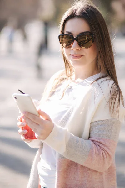 Mooie vrouw met telefoon en drankjes limonade buiten. Jonge blogger brengt tijd door in park — Stockfoto