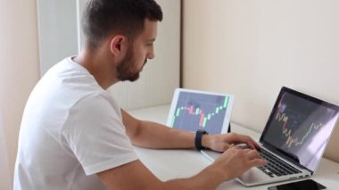 Bilgisayardaki ve tabletteki finans tabletine bakan adam, borsacı, evden yatırım yapan. Genç adam yatırımlarını izliyor. Hırslı iş adamı.
