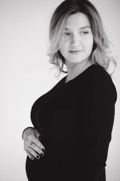 Retrato de mujer embarazada en estudio sobre fondo blanco. Hermosa futura madre puso sus manos sobre su vientre. Foto en blanco y negro — Foto de Stock