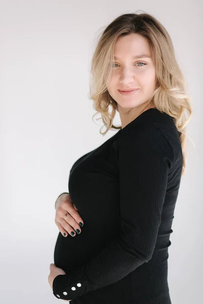 Retrato de mujer embarazada en estudio sobre fondo blanco. Hermosa futura madre puso sus manos sobre su vientre. Cabello suelto — Foto de Stock