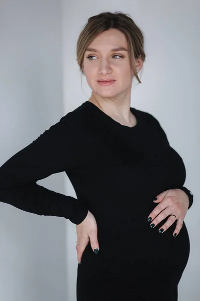 Elegante mujer embarazada en hermosa negro de maternidad drees poner la mano en el vientre en el estudio. Fondo blanco — Foto de Stock