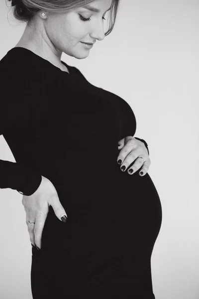 Close up portrait of gogreous pregnant woman in bkack dress hold her hand on belly and looks down — Stock Photo, Image
