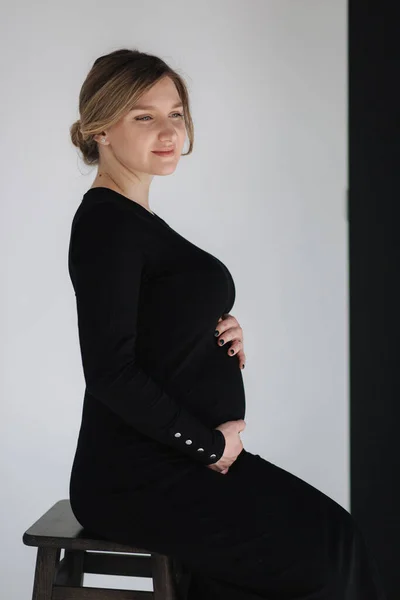Close up retrato de mulher grávida gogreous em vestido bkack segurar a mão na barriga e olha para baixo — Fotografia de Stock