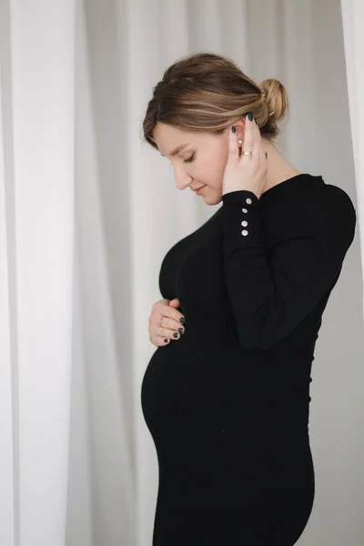 Schwangere im schwarzen Kleid gehen durch die weißen Vorhänge — Stockfoto