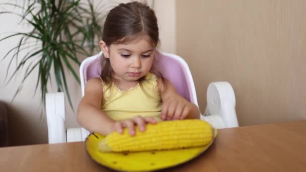 Urocza dziewczynka położyła rękę na kukurydzy i poprosiła mamę o jedzenie. Gotowana na gorąco kukurydza na żółtym talerzu. Dzieciak czeka na lunch. — Wideo stockowe