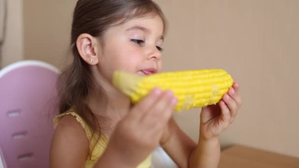 Proces małej dziewczynki jedzącej świeżą kukurydzę w domu. Urocze dziecko siedzi na stole i je kukurydzę apetyt — Wideo stockowe