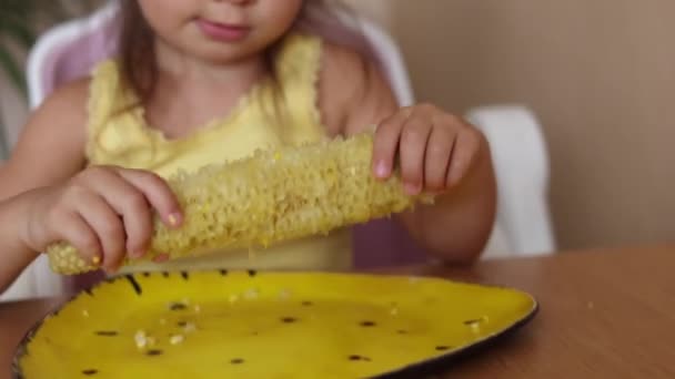 Bonito peixe menina comendo milho e limpa a boca. Criança adorável em camisa amarela coloca baloiço de milho na placa amarela. Humor de verão em casa. Foco no milho — Vídeo de Stock