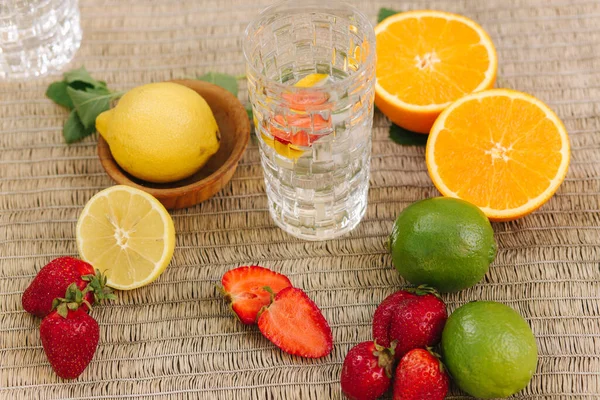 Un vaso alto de agua con hielo. Naranjas, limones, lima y fresa en rodajas — Foto de Stock