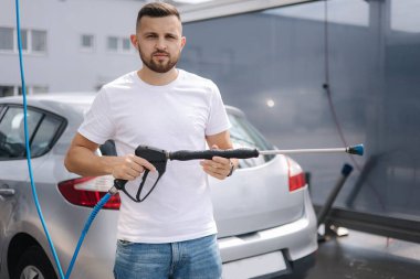 Kendini yıkama istasyonunda yakışıklı bir adamın portresi. Islak gri arabanın arka planı