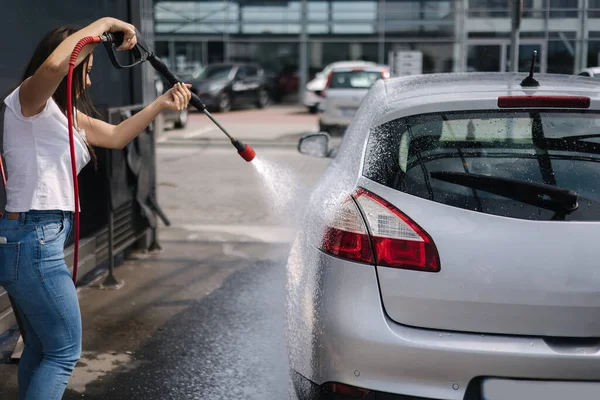 Kendi servis arabasında arabasını temizleyen genç bir kadının arka görüntüsü. Jet spreyli kadın yıkama. Arabada beyaz köpük — Stok fotoğraf