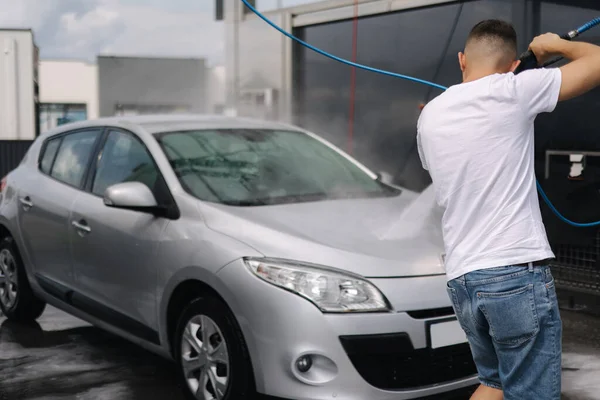 Jet püskürtücüyle arabasını temizleyen genç bir adamın arka görüntüsü. Otomobil yıkama servisi. — Stok fotoğraf
