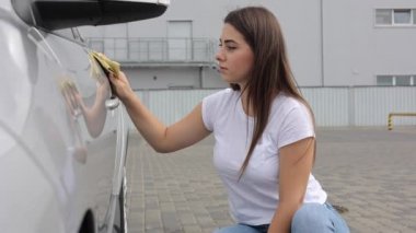 Çekici, mutlu, kadın sürücü arabasını oto yıkamada bez kullanarak siliyor.