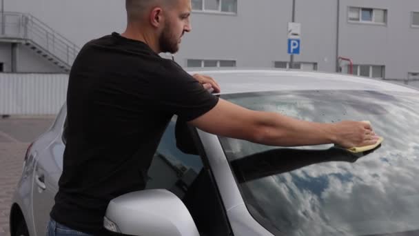 Un uomo pulisce un parabrezza della sua auto con uno straccio in uno showroom in un autolavaggio self-service — Video Stock