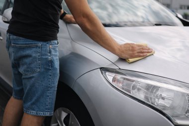 Yakışıklı bir adamın orta seçimi, oto yıkamacıdaki bir galeride bir bez parçasıyla araba siliyor. Arka plan