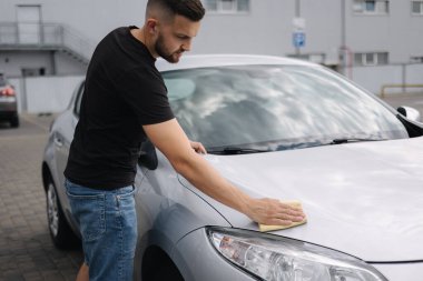 Adamın eli arabasının farlarını halıyla siliyor. self-servis araba yıkama. Açık hava.