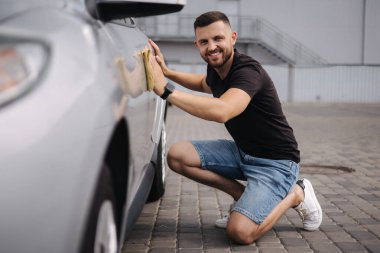 Yakışıklı bir adam galeride bir bez parçasıyla araba yıkama servisinde araba siliyor.