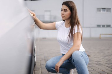 Çekici, mutlu kadın sürücünün ön görüntüsü. Arabasını özel bir bez parçasıyla yıkıyor.