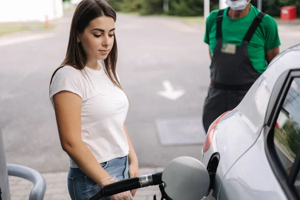 Kobieta tankuje na stacji benzynowej. Kobieta napełnia benzyną benzynę benzynową w samochodzie. Koncepcja cen benzyny. Pracownik stacji benzynowej stoi w tle — Zdjęcie stockowe