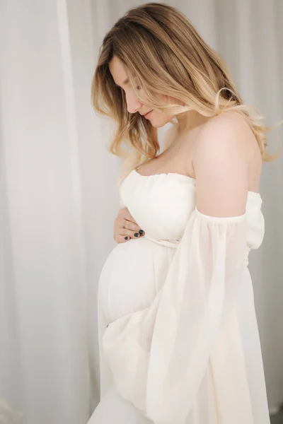Beautiful portrait of pregnant woman in white dress. Concept of perfect pregnancy. Woman put her hand on belly. Future mother is waiting for baby — Zdjęcie stockowe
